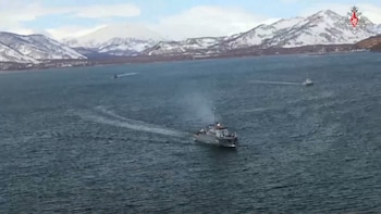 Vista aérea de tres buques militares pequeños navegando en aguas oscuras y agitadas, con montañas cubiertas de nieve al fondo