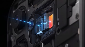Primer plano de los componentes internos de una cámara periscópica de celular, con haces de luz azul reflejándose en un prisma hacia un sensor naranja.
