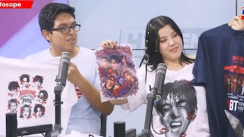 Un hombre y una mujer muestran estampados y camisetas con la imagen del grupo surcoreano BTS frente a dos micrófonos de estudio