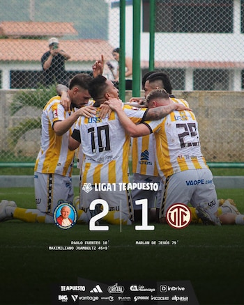 Cinco futbolistas de Juan Pablo II, con camisetas a rayas amarillas y blancas, se abrazan en el campo celebrando un gol, con el marcador 2-1 superpuesto