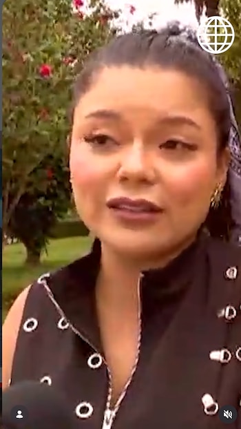 Primer plano de Briela Cirilo con un chaleco negro y el cabello recogido mientras habla frente a un micrófono en un parque