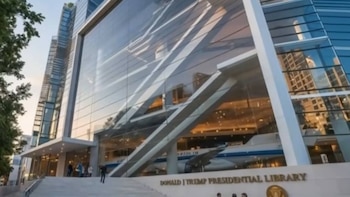 Exterior de la Biblioteca Presidencial Donald Trump, un edificio moderno con fachada de vidrio. Un avión blanco se ve dentro; el nombre de la biblioteca en la base