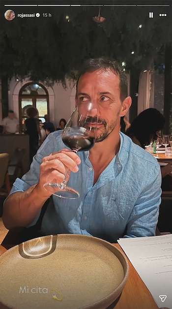 Primer plano de Luis Brandoni, un hombre de mediana edad con barba, olfateando una copa de vino tinto en un restaurante