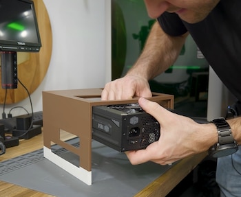 Manos de una persona instalando una fuente de poder negra marca Cooler Master V850 en un gabinete marrón con base blanca sobre una mesa de trabajo