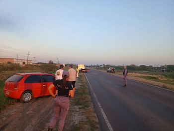 Agentes de policía, civiles y un automóvil rojo a la orilla de una carretera pavimentada con una grúa al fondo