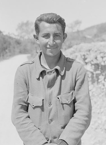 Fotografía en blanco y negro de un hombre joven que sonríe y viste una chaqueta con bolsillos en una zona rural