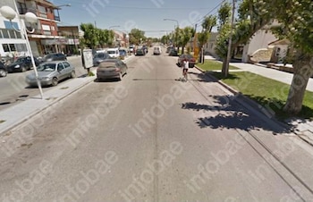 Una calle asfaltada con vehículos estacionados a un lado, árboles a la derecha y una persona que circula en bicicleta