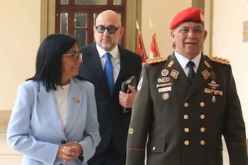 Delcy Rodríguez, con chaqueta azul claro, sonríe junto a un hombre con traje oscuro y gafas, y GJ Gustavo González López, en uniforme militar y boina roja
