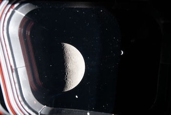Desde el lado oculto de la Luna , los astronautas tomaron esta fotografía a través de una de las ventanas de la nave Orión. En ella se ve una Luna en cuarto creciente en primer plano, con una Tierra brillante pero diminuta al fondo. (NASA)