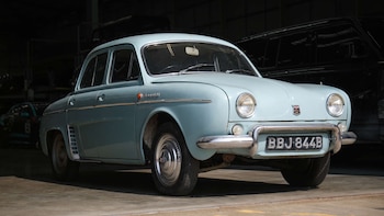 Automóvil clásico de color azul claro con matrícula BBJ 844B estacionado dentro de un garaje junto a otros vehículos