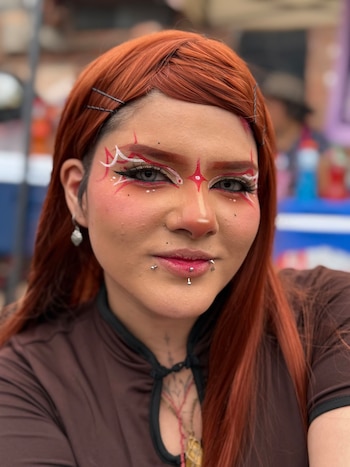 Primer plano de una mujer de cabello pelirrojo con maquillaje artístico rojo en el rostro y perforaciones en los labios