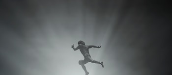 Estatua de futbolista en silueta contra un cielo claro con rayos de luz. El jugador está en una pose dinámica como si estuviera driblando un balón