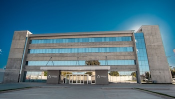 Vista exterior frontal del Sanatorio de la Trinidad Neuquén, un edificio moderno de hormigón y vidrio con varias plantas, bajo un cielo azul brillante y un aparcamiento vacío