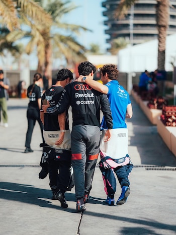 Franco Colapinto (camiseta azul Alpine F1) camina de espaldas con dos compañeros en una pista. Visten ropa de equipo y llevan trajes de carrera
