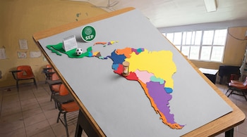 Mapa conceptual de América Latina en una mesa. Países en diversos colores; México con calendario, balón y logo SEP. Perú con reloj de arena. Fondo de aula de dibujo.