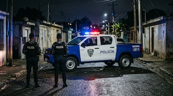 Dos agentes policiales de espaldas frente a una patrulla con balizas encendidas en una calle residencial nocturna.