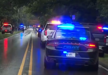 Una fila de vehículos policiales con luces azules y rojas encendidas en una carretera oscura y mojada con doble línea amarilla