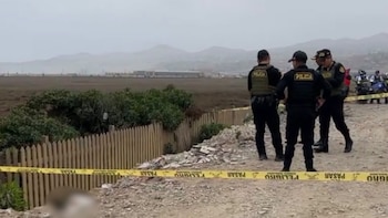 Agentes de policía custodian un terreno acordonado con cinta amarilla junto a una cerca de madera y un área descampada