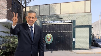 Un hombre vestido de traje oscuro y corbata azul sonríe y levanta dos dedos. Detrás se ve un portón de metal negro con el letrero 'S.S. PNP EP BARBADILLO-CEINPOL'.