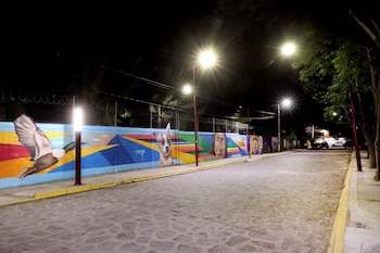 Calle empedrada de noche con múltiples farolas LED encendidas, iluminando un mural colorido en una pared a la izquierda con figuras de animales y rostros
