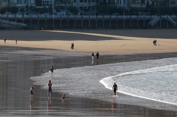 Bañistas y paseantes disfrutan de un día soleado en la playa de la Concha de San Sebastián. (Juan Herrero/EFE)
