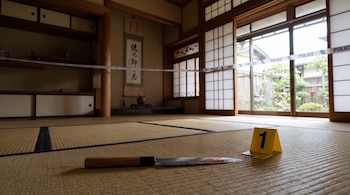 Cuchillo yanagiba ensangrentado y un marcador forense número uno sobre un suelo de tatami, con cinta policial en una casa tradicional japonesa.
