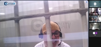 Captura de pantalla de una videollamada con un hombre con auriculares tras unos barrotes y miniatura de los asistentes a la derecha
