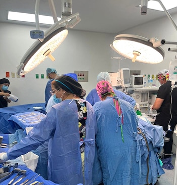 Un equipo de cirujanos y personal de enfermería en un quirófano, con mesas de instrumentos estériles y luces quirúrgicas encendidas