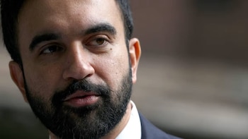 Primer plano del rostro de Zohran Mamdani, mostrando su mirada, nariz y boca con barba oscura. Viste camisa blanca y saco oscuro