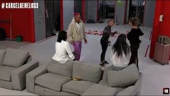 Cinco personas en un estudio con paredes rojas y mobiliario gris. Dos mujeres sentadas en sofás y tres de pie, incluyendo un hombre con cabello rosa. Hay un hashtag y +18 visible