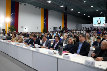 Decenas de personas sentadas en mesas albergadas en un auditorio con varias banderas de Venezuela al fondo