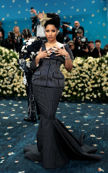 Sobre el hombro izquierdo, Nicki Minaj lució una estructura ornamental de gran tamaño con flores textiles en negro, blanco y azul, combinada con un moño dorado semitransparente en el peinado alto