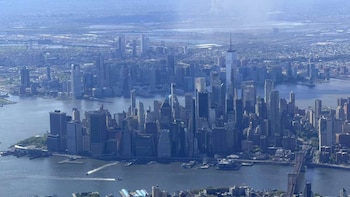 Vista aérea de una gran zona urbana con numerosos rascacielos, incluido el One World Trade Center, rodeada de agua y puentes