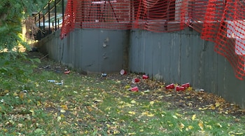 Vasos plásticos rojos y latas metálicas caídos sobre la hierba junto a una pared de hormigón y una cerca naranja