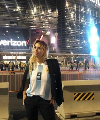 Wanda Nara viste una camiseta de fútbol a rayas celestes y blancas con el número nueve, saco negro y pantalón oscuro frente a un estadio iluminado