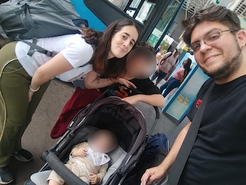 Selfie de una mujer (Victoria), un hombre y un bebé en un cochecito. La mujer lleva mochila y el hombre gafas. Hay un niño más atrás