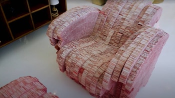 Un sillón club y un taburete, ambos construidos con múltiples capas de material que simula rebanadas de carne de cerdo, en un interior blanco