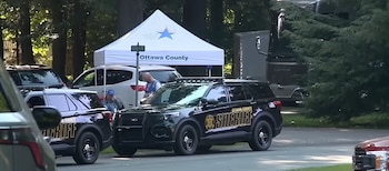 Dos SUV policiales del Sheriff, una carpa blanca con el logo del Cuerpo de Reserva Médica y texto Ottawa County, personas, árboles