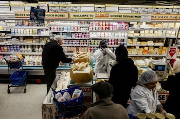 Clientes y personal en un departamento de quesos de supermercado, con estantes llenos de quesos, yogures y productos lácteos