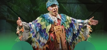 Un hombre con traje de plumas y hojas de colores, sombrero de plumas azul, maquillaje facial y una flauta de pan. Tiene los brazos extendidos