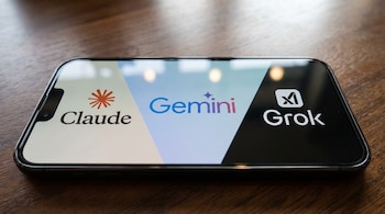 Un smartphone negro horizontal sobre una mesa de madera. En la pantalla se ven los logos de Claude a la izquierda, Gemini en el centro y Grok a la derecha.