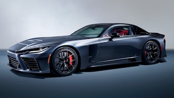Automóvil deportivo gris oscuro con diseño aerodinámico, llantas negras, pinzas de freno rojas y asientos interiores rojos, exhibido en estudio