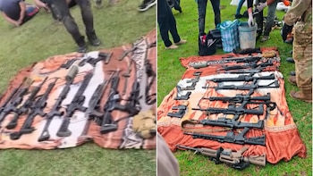 Un despliegue de fusiles, pistolas, cargadores y otro armamento sobre una manta en el pasto, con personas paradas alrededor