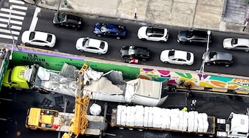 Vista aérea de un camión accidentado con la estructura colapsada, una grúa amarilla y automóviles en una calle.