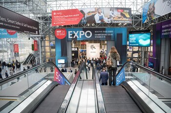 Vista aérea del interior de un centro de convenciones con escaleras mecánicas, muchas personas y grandes carteles publicitarios de la NRF '24 Retail's BIG Show