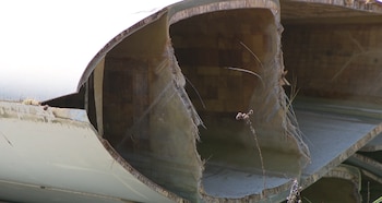 Primer plano de una sección rota de una pala de aerogenerador con la estructura interna de capas de material compuesto de color beige y bordes deshilachados