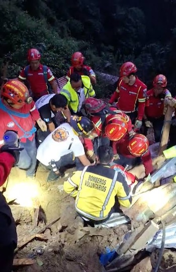 Integrantes de un cuerpo de rescate con cascos, linternas y chaquetas reflectantes trabajan de noche en un terreno oscuro con escombros