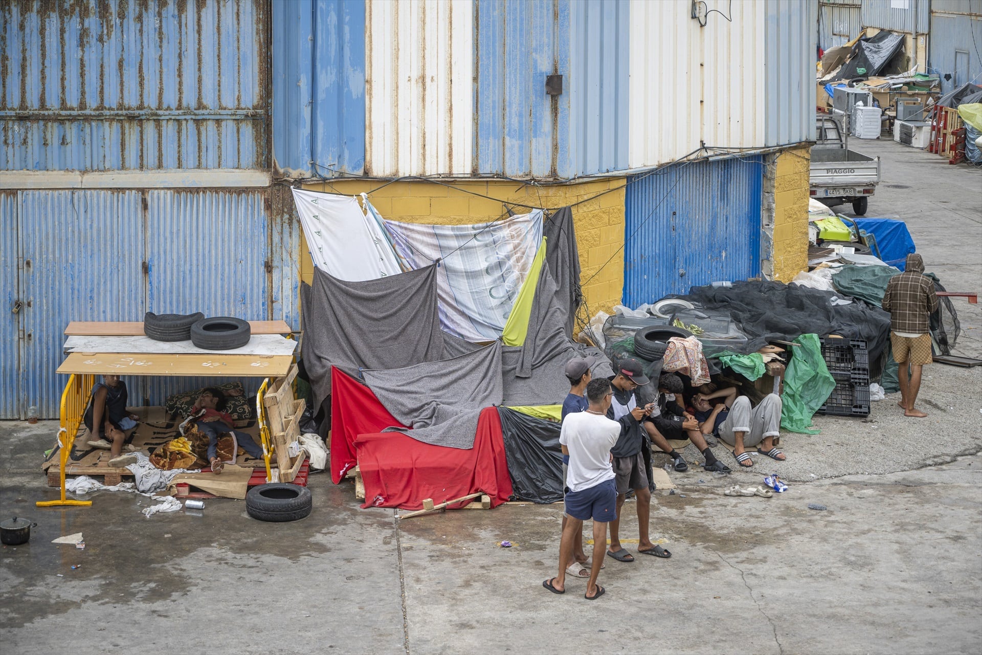 Varios migrantes se protegen de la lluvia con telas y lonas en la ciudad autónoma. (Europa Press)