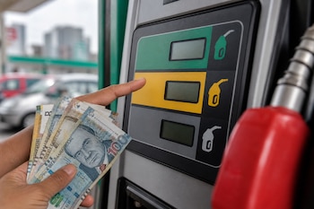 Manos sostienen billetes peruanos frente al panel de botones de un surtidor de combustible con una manguera roja en primer plano.