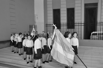 Figuras en miniatura de estudiantes en uniforme escolar sostienen una bandera en una maqueta en blanco y negro